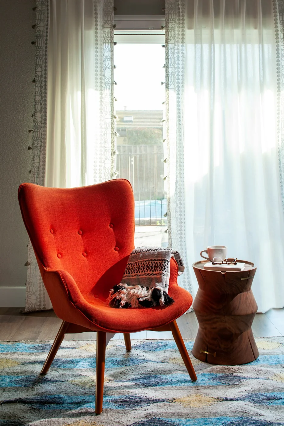 A comfortable orange armchair beside a window with soft light, a blanket and a cup of tea